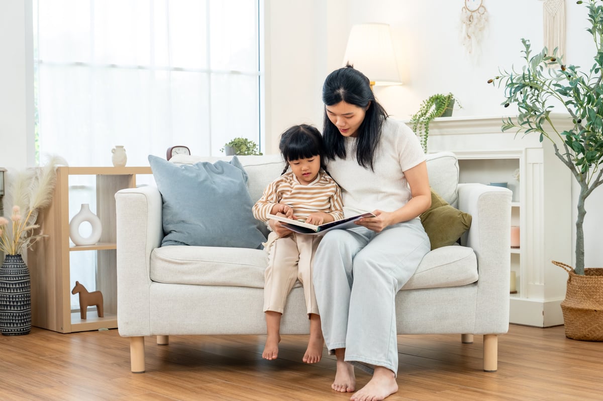 Parent and young child reading a picture book together on a sofa