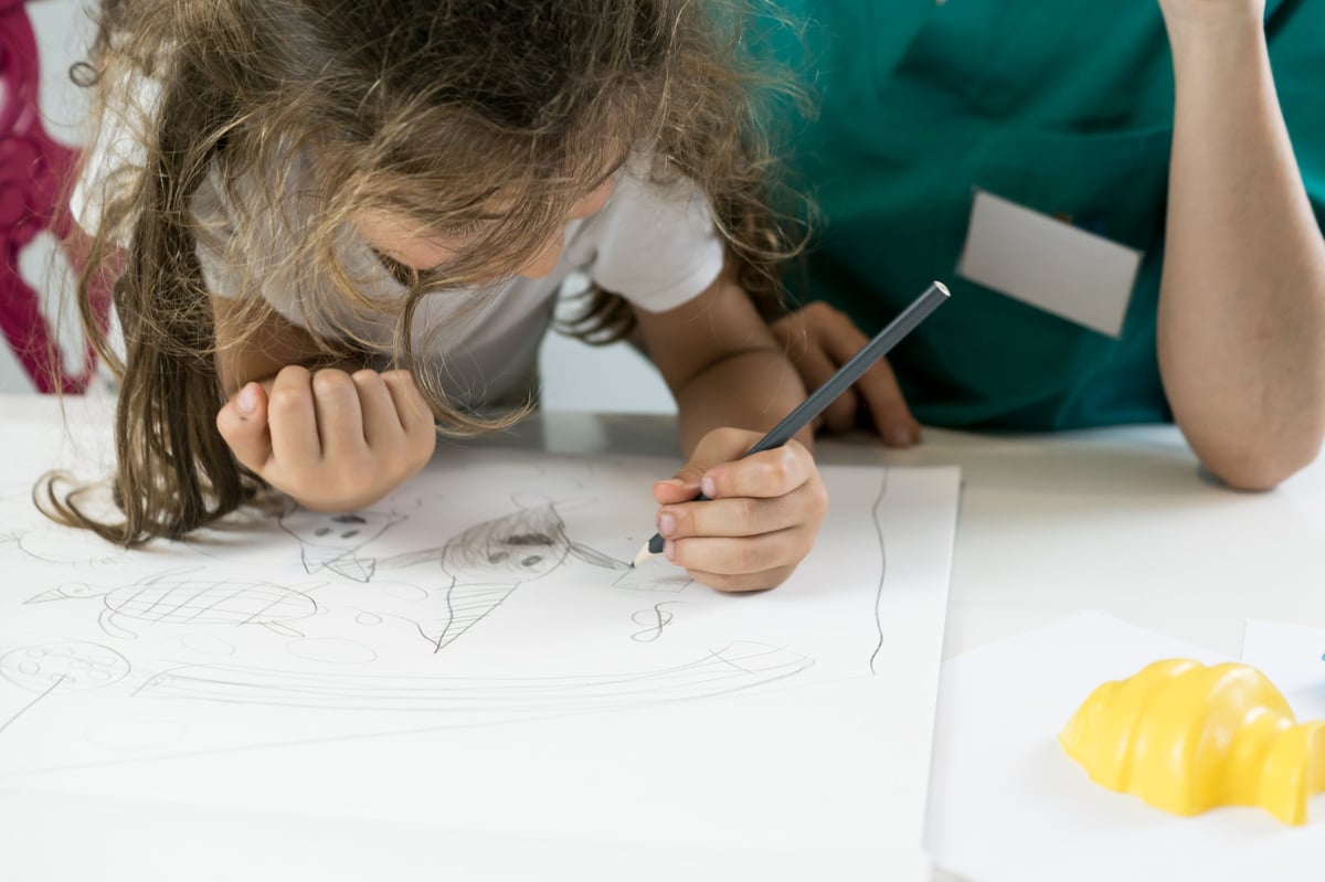 Girl leaning over a desk concentrating while drawing with a pencil