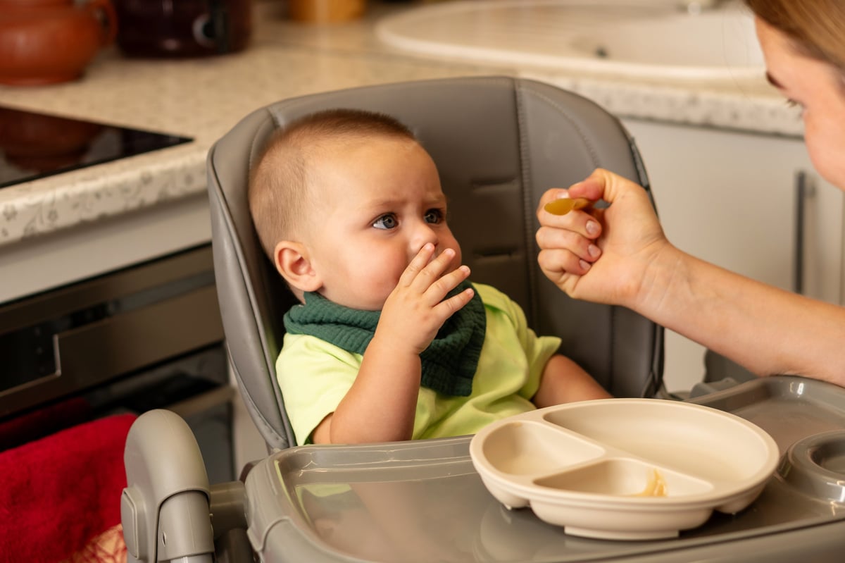 Baby in a high chair being offered a spoon during a meal at home