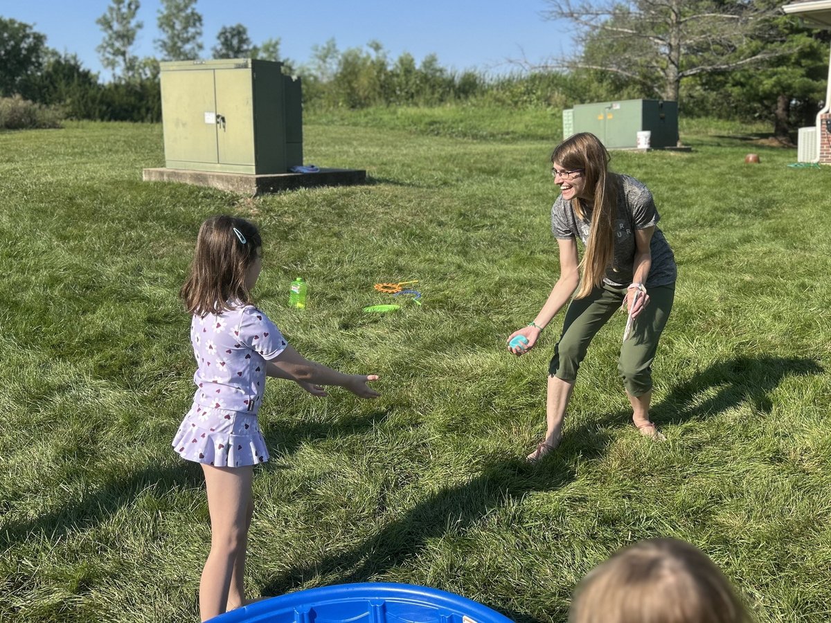 Therapist and child playing a catching game on the grass outside the clinic, outdoor pediatric occupational therapy