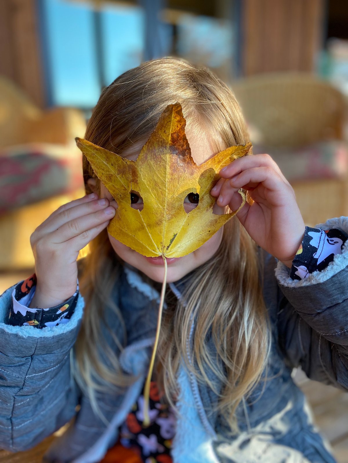 Child holding a decorated autumn leaf over her face — a playful fall speech and language activity in Lawrence, KS