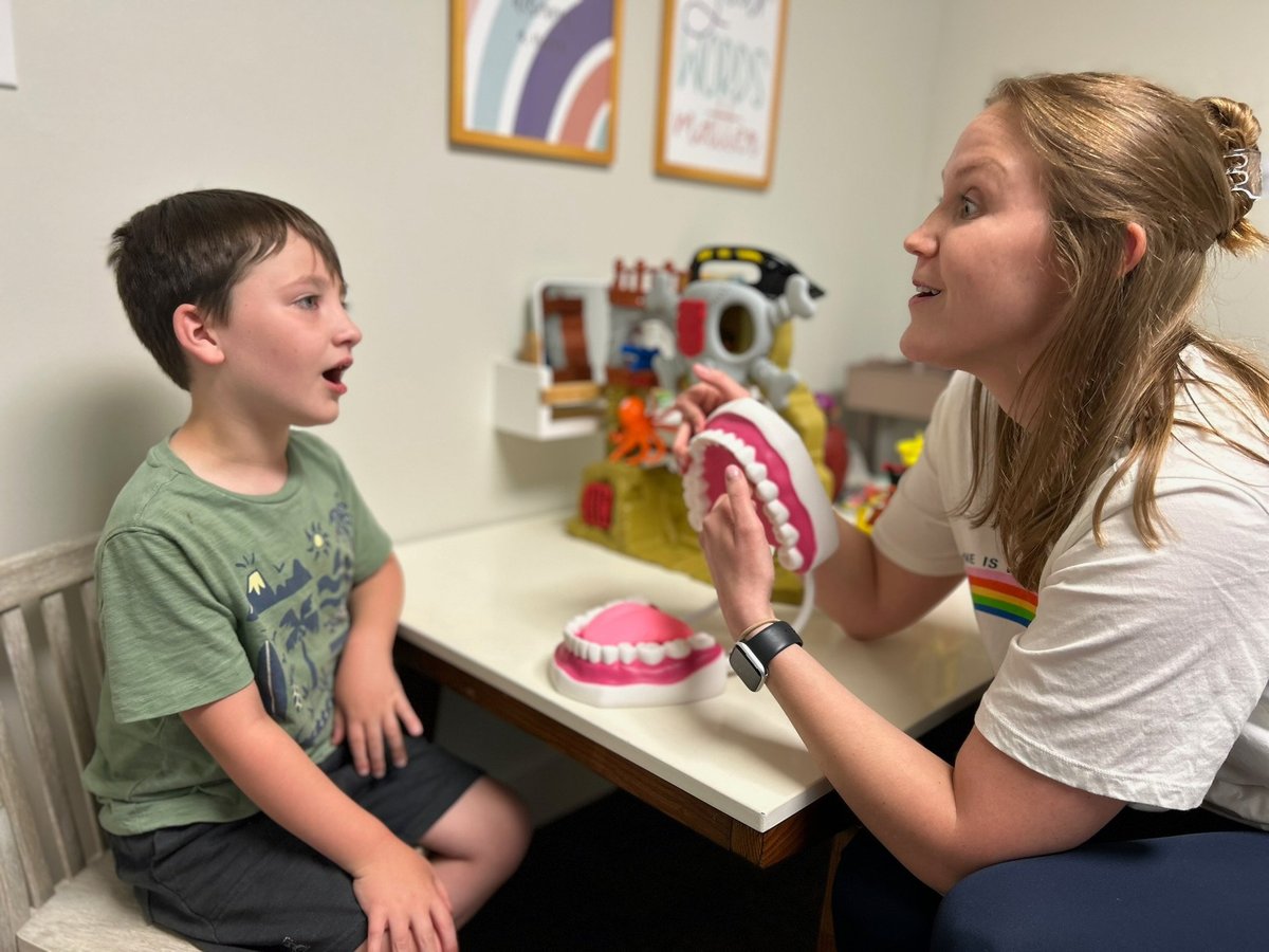 Speech-language pathologist showing a young boy a large mouth model so he can see how speech sounds are made during articulation therapy