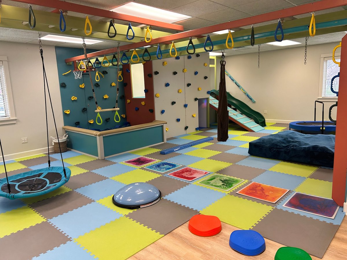 Wide view of the custom-built New Heights Therapy sensory gym with foam tile floor, climbing wall, monkey bars and slide