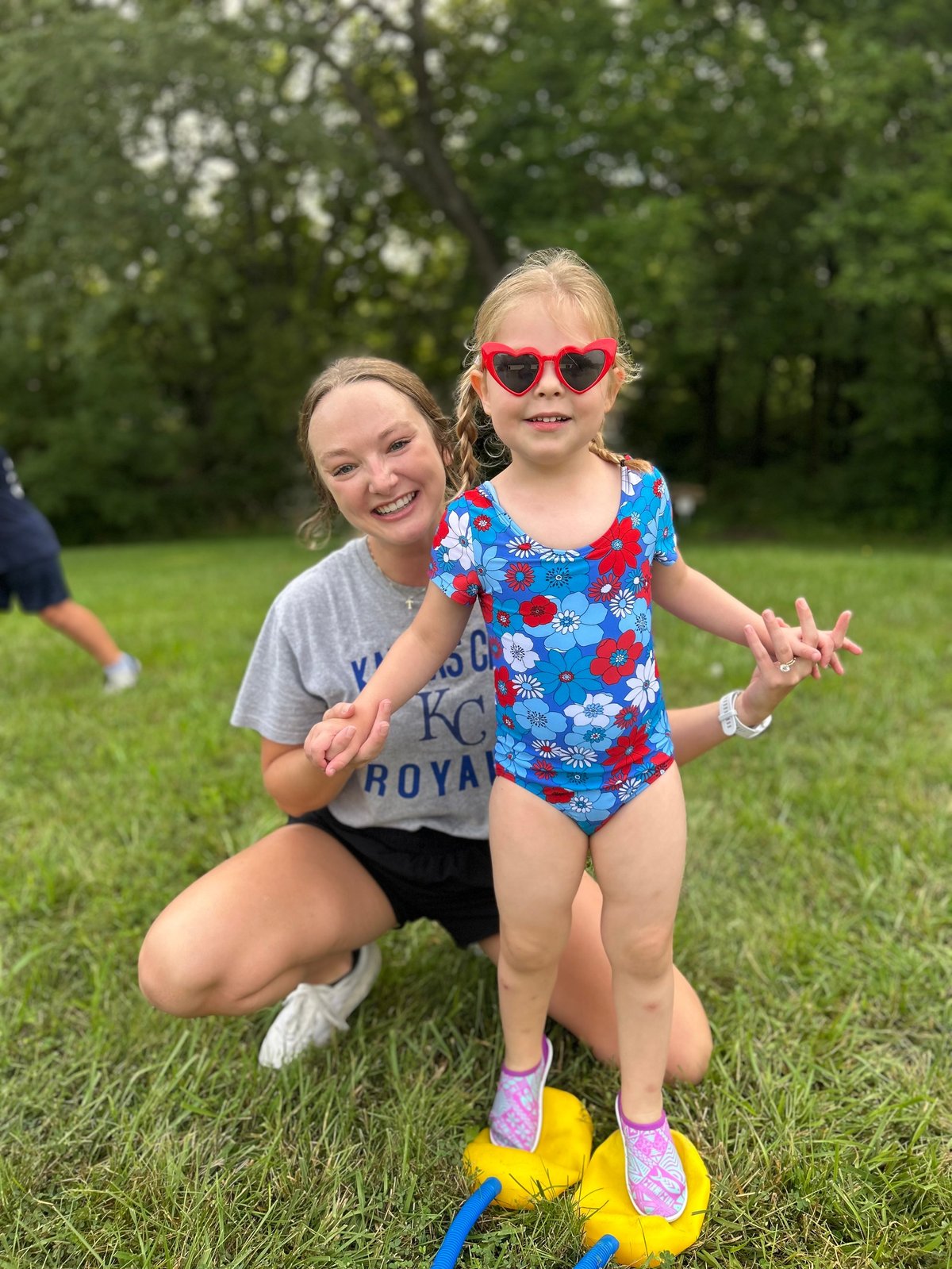 Young girl in a flower swimsuit balancing on stepping stones with her speech therapist during outdoor speech therapy in Lawrence or Topeka, Kansas