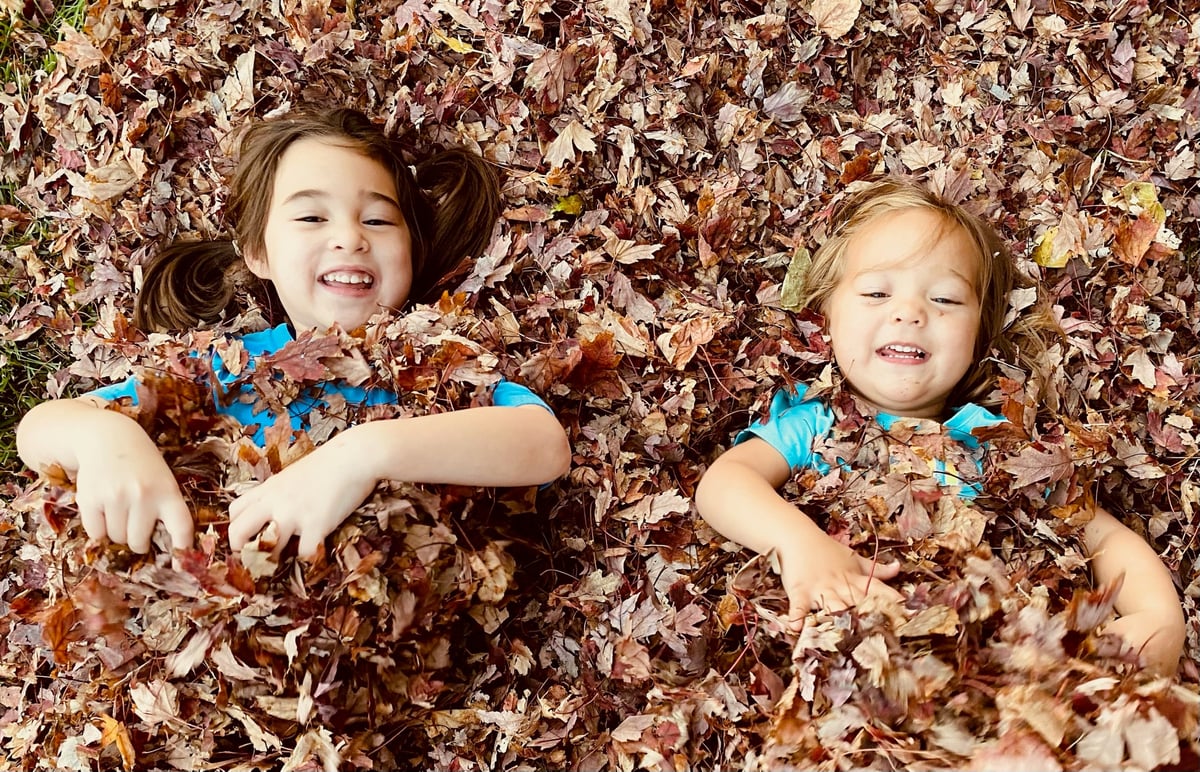 Two young children in colorful shirts lying in a pile of autumn leaves and smiling up at the camera during outdoor pediatric therapy with New Heights Therapy.