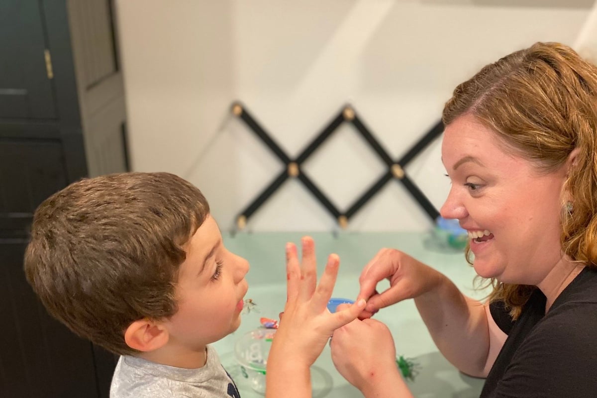 Woman and young boy examining hands together indoors with decorative wall art in background.