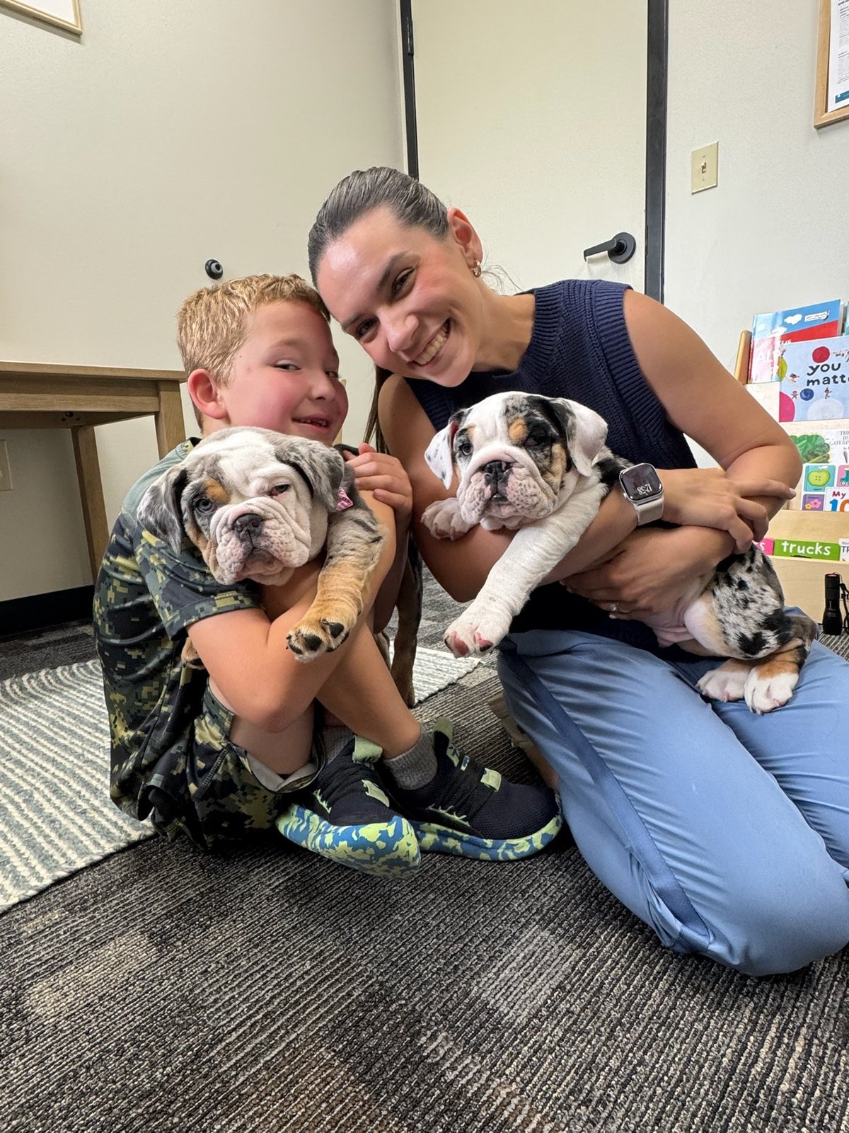 Speech therapist and a young boy holding two bulldog puppies in a therapy room at New Heights Therapy