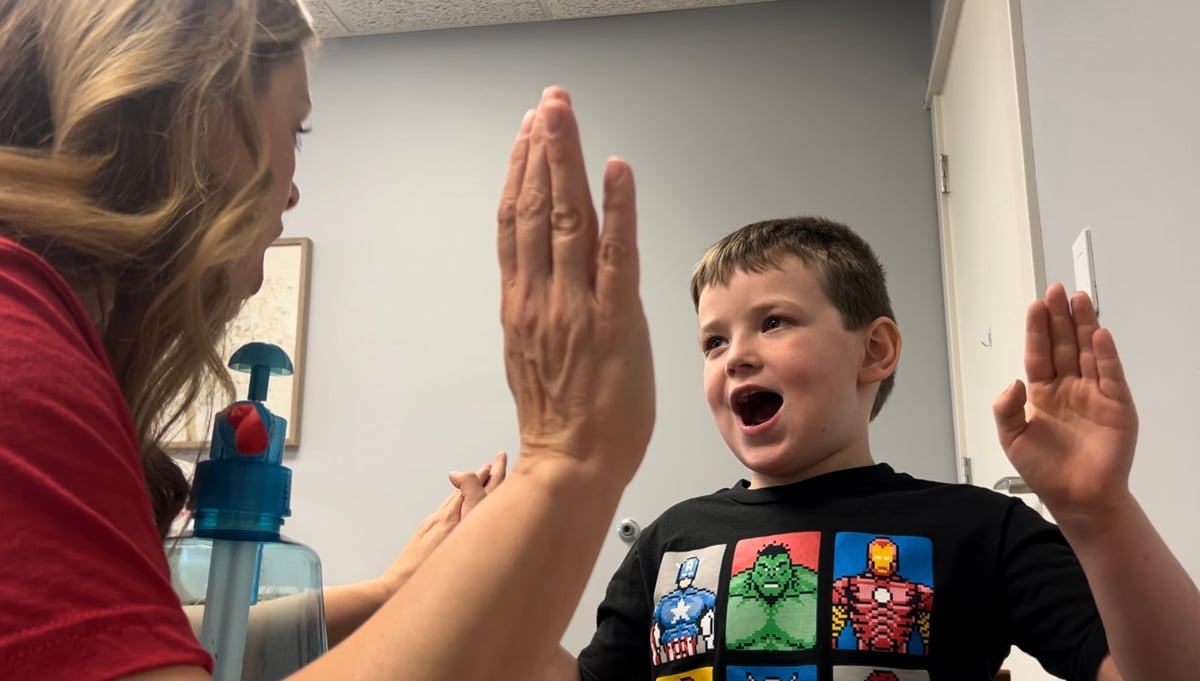 Young boy sharing a celebratory high-five with his speech therapist after a successful speech therapy activity