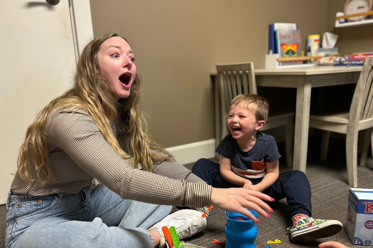 Woman and young child playing with toys together on the floor, both appearing happy and engaged during playtime indoors.