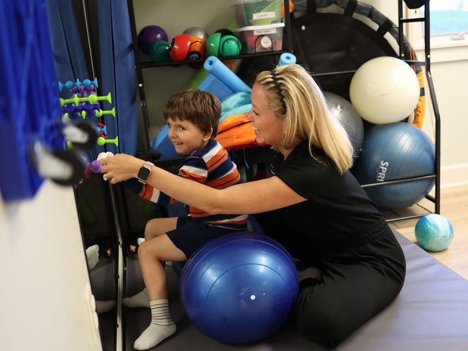 Child therapy ball sitting balance in pediatric physical therapy, a therapist steadying a child on a blue stability ball