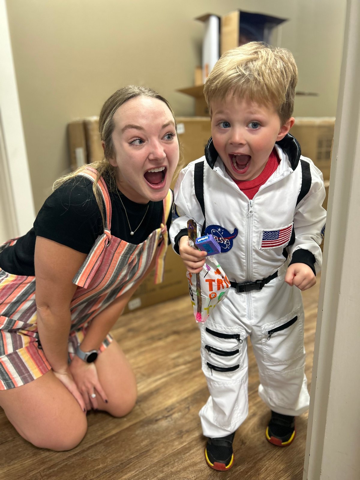 Speech therapist kneeling beside a toddler in an astronaut costume, smiling during a playful speech therapy session in Kansas
