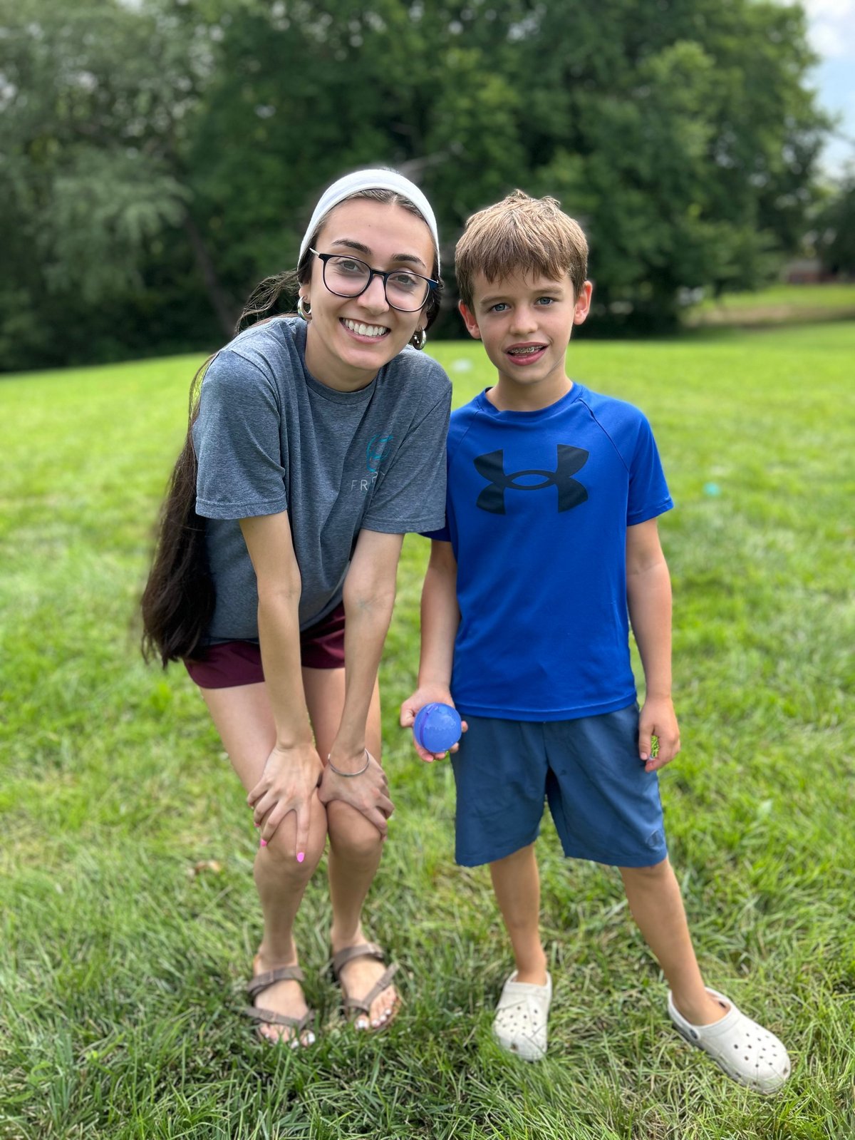 Speech therapist and a young boy smiling together in a park, celebrating progress made in speech therapy