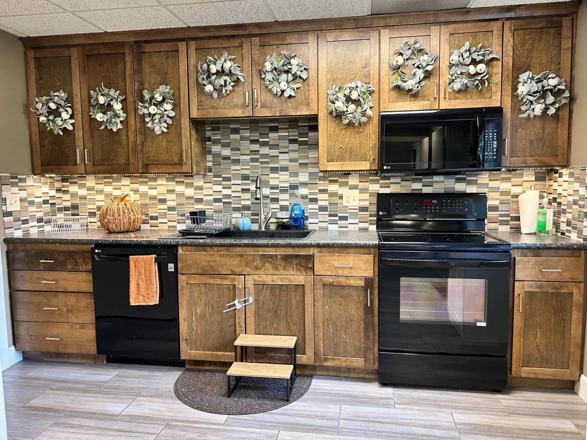 Full teaching kitchen at New Heights Therapy in Lawrence, Kansas, with wood cabinetry, black appliances, a tiled backsplash and floral accents — where pediatric occupational and feeding therapists help children cook, pour, stir and prepare real food