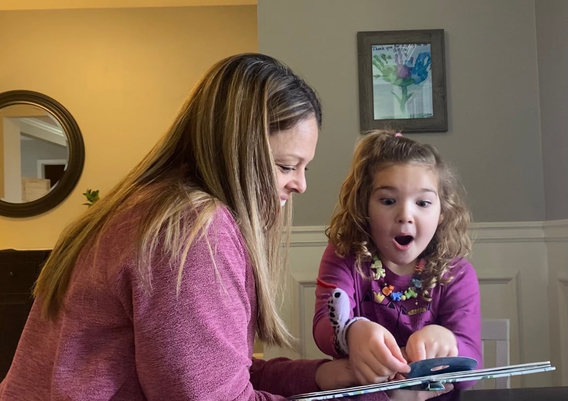 Pediatric speech-language pathologist and a young child in a purple outfit reading a book together with excitement at New Heights Therapy in Kansas