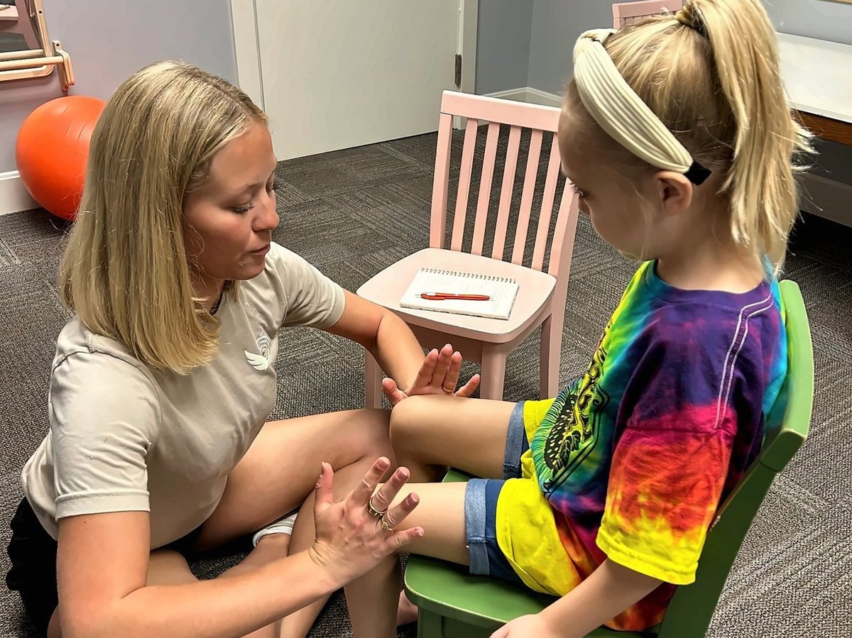 Pediatric physical therapist checking a child's knee and arm strength during an assessment at New Heights Therapy in Kansas