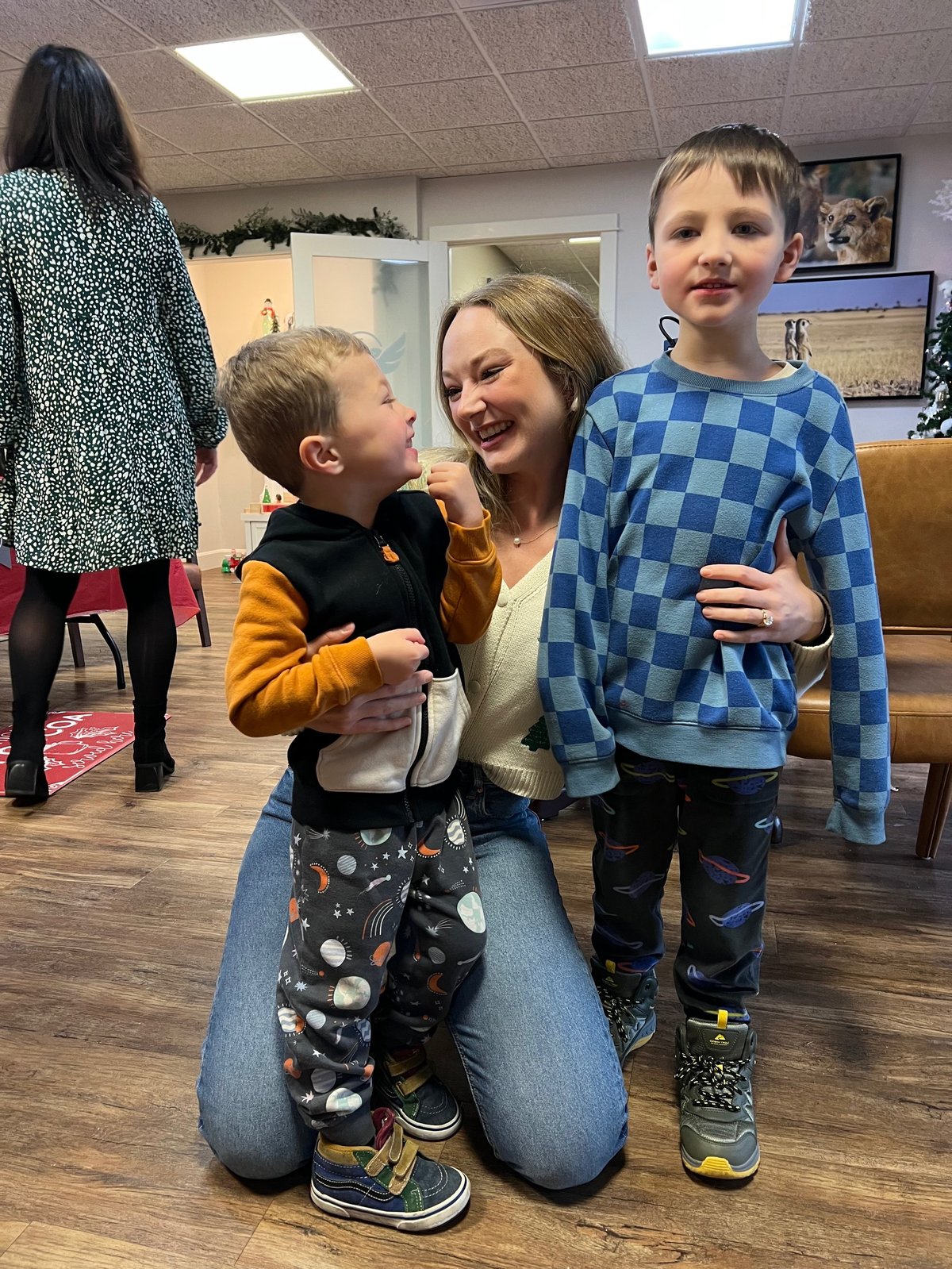 Speech therapist kneeling with two young boys in the therapy room, smiling together during pediatric speech therapy in Kansas