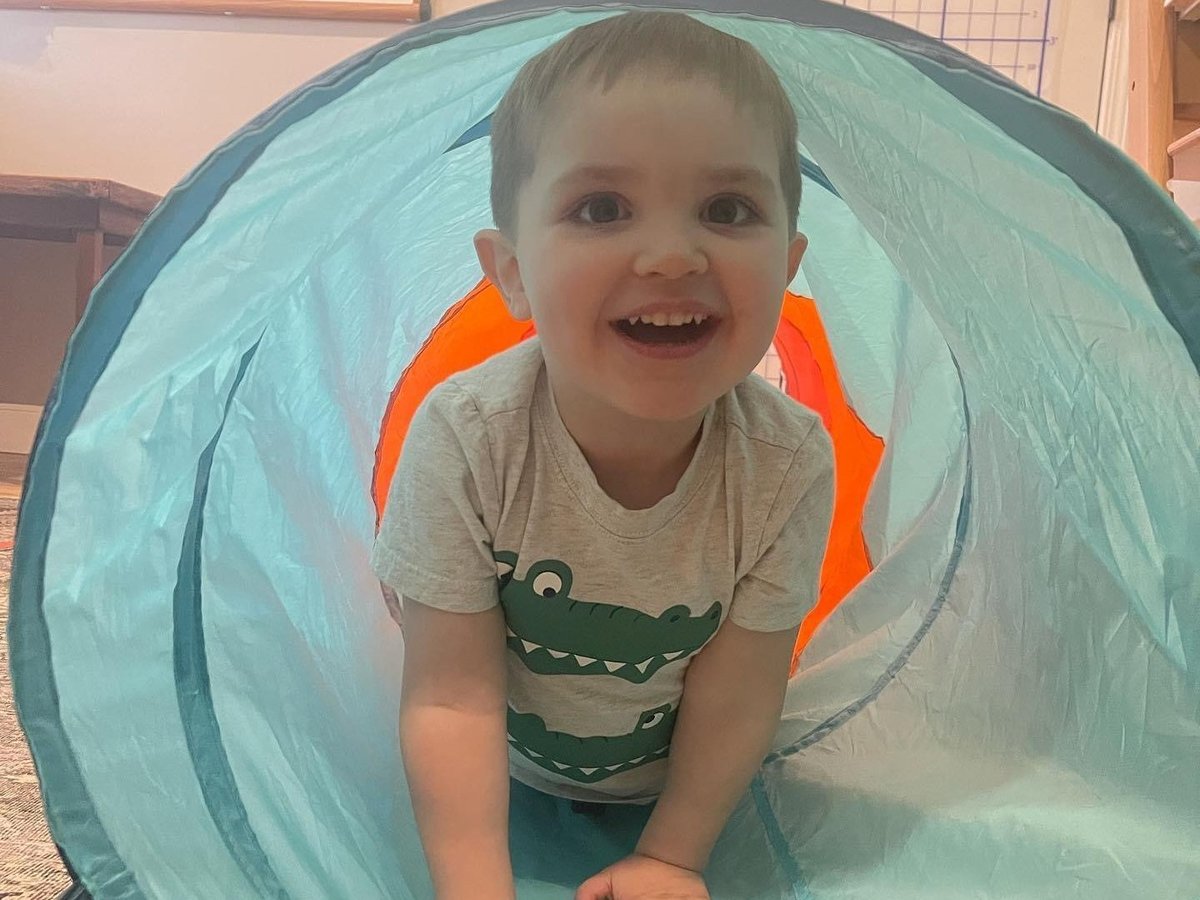 Toddler smiling inside a light blue play tunnel, crawling practice in pediatric occupational therapy
