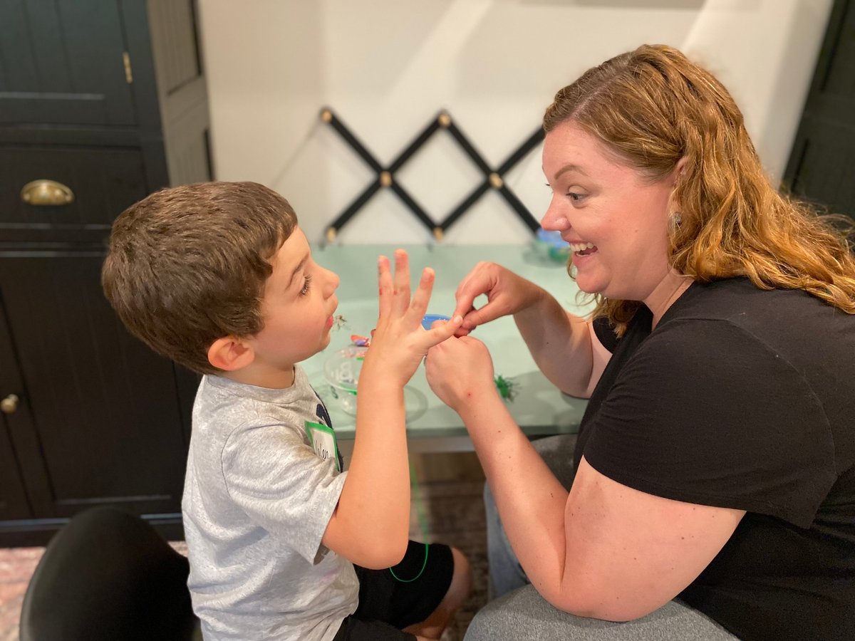 Speech therapist and a young boy laughing while playing a hand game that builds turn-taking and social communication