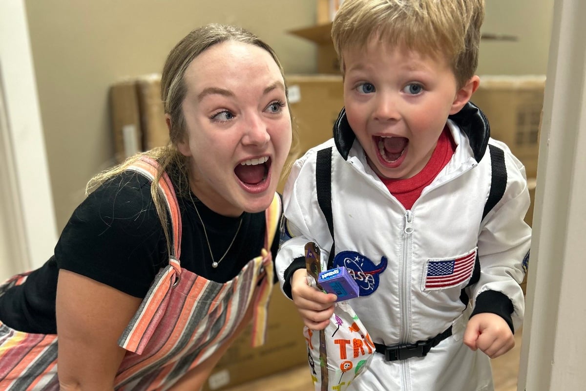 A woman and young boy smile excitedly at the camera, with the boy dressed in a NASA astronaut costume.