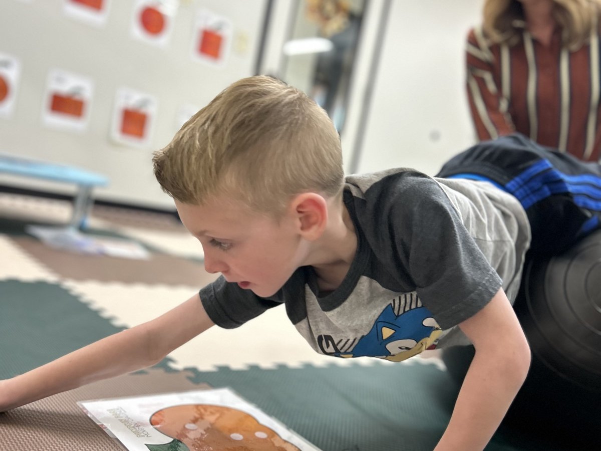 Child prone over a therapy ball working on a puzzle, building core strength during occupational therapy at New Heights Therapy in Lawrence and Topeka, Kansas