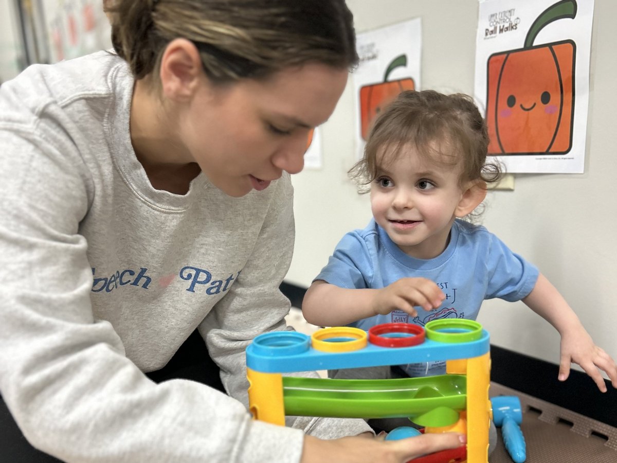 Speech therapist and a toddler playing with a colorful stacking ring toy, encouraging early language and joint attention in speech therapy