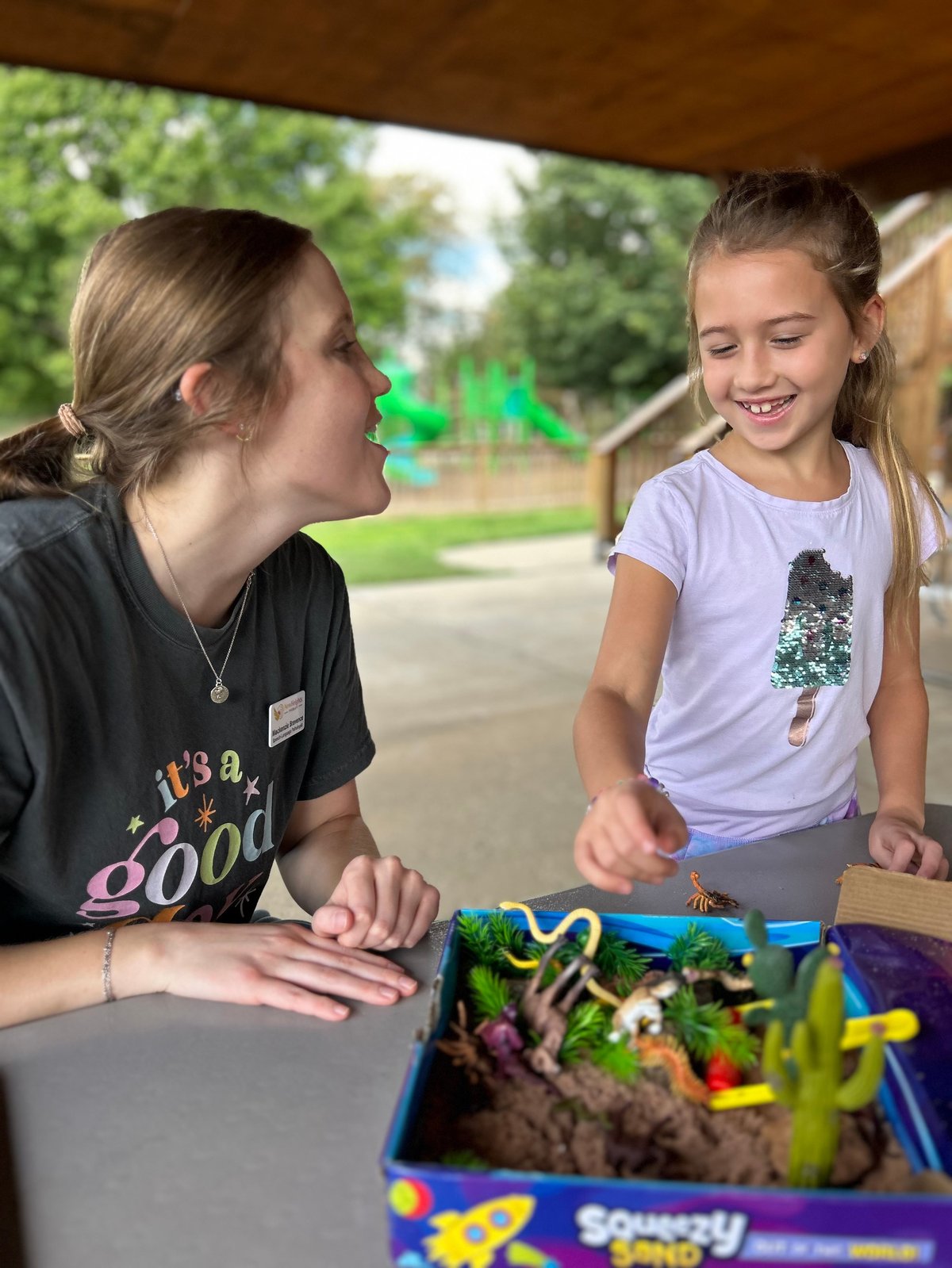 Speech therapist and a girl from Lawrence, KS exploring succulents and toy dinosaurs in a sensory sand bin — hands-on vocabulary building in speech therapy