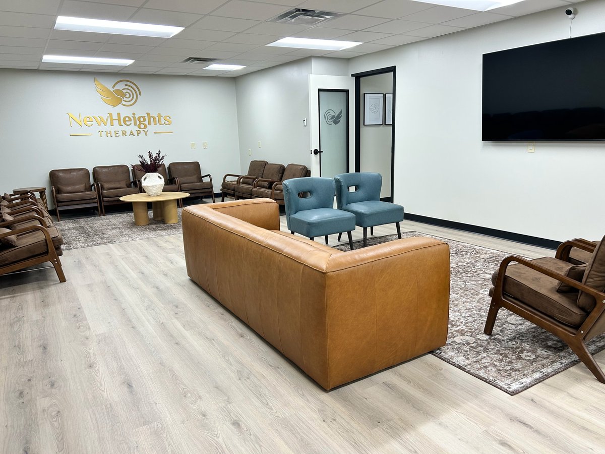 Modern therapy office waiting room with leather sofas, blue armchair, wooden flooring, and New Heights Therapy signage