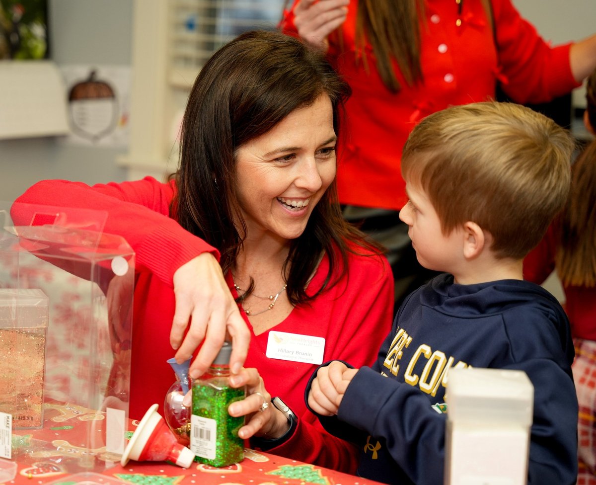 Therapist and a young boy working side by side on a craft activity at a table during a family-centered session at New Heights Therapy.