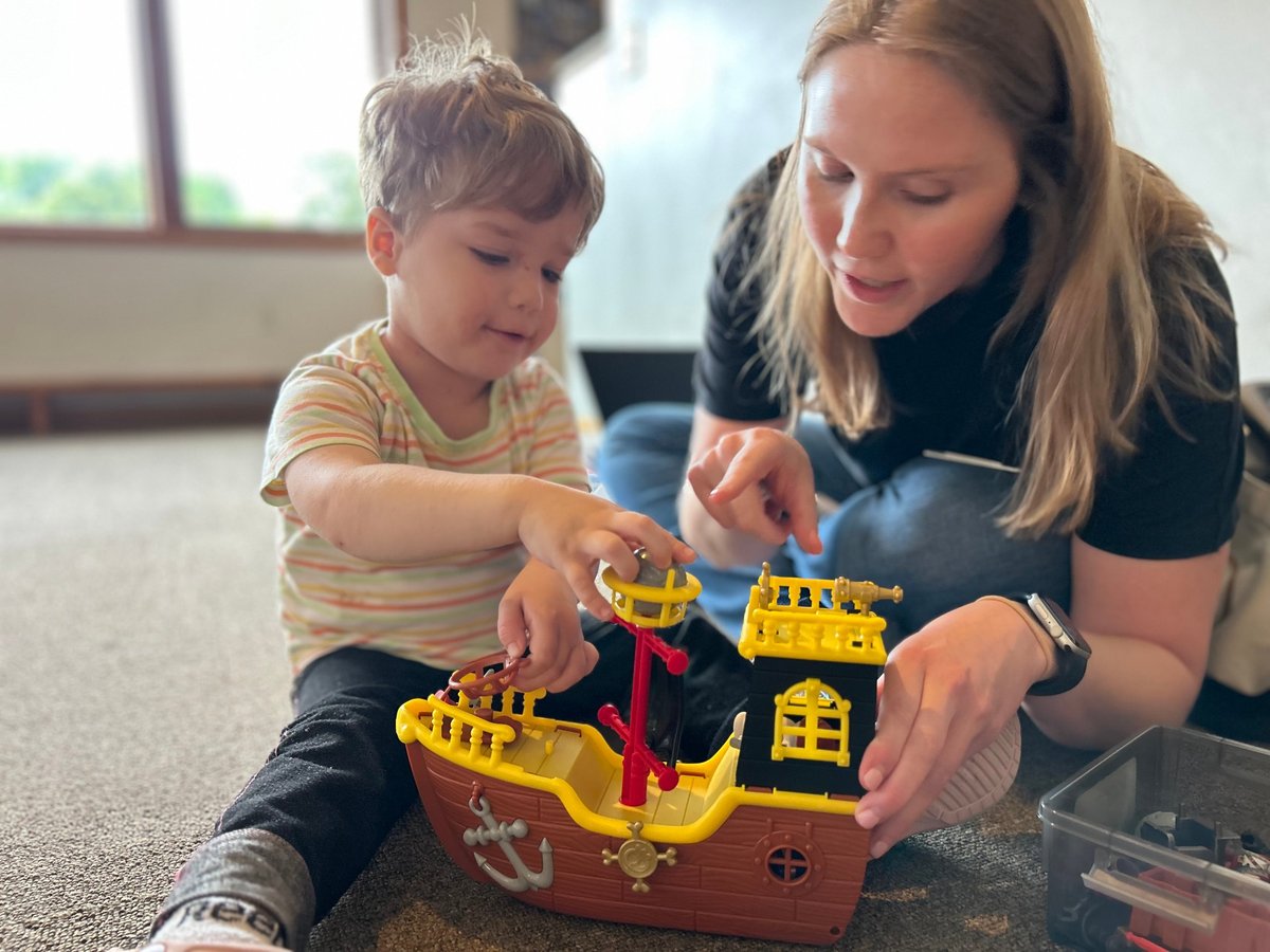 Speech therapist and child playing with a toy pirate ship on the floor, using pretend play to build vocabulary in speech therapy