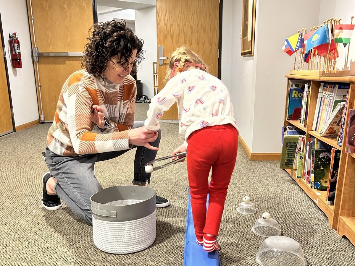 Child balancing on a beam and planning each step while a therapist kneels beside a basket of props, motor planning work in a New Heights Therapy session
