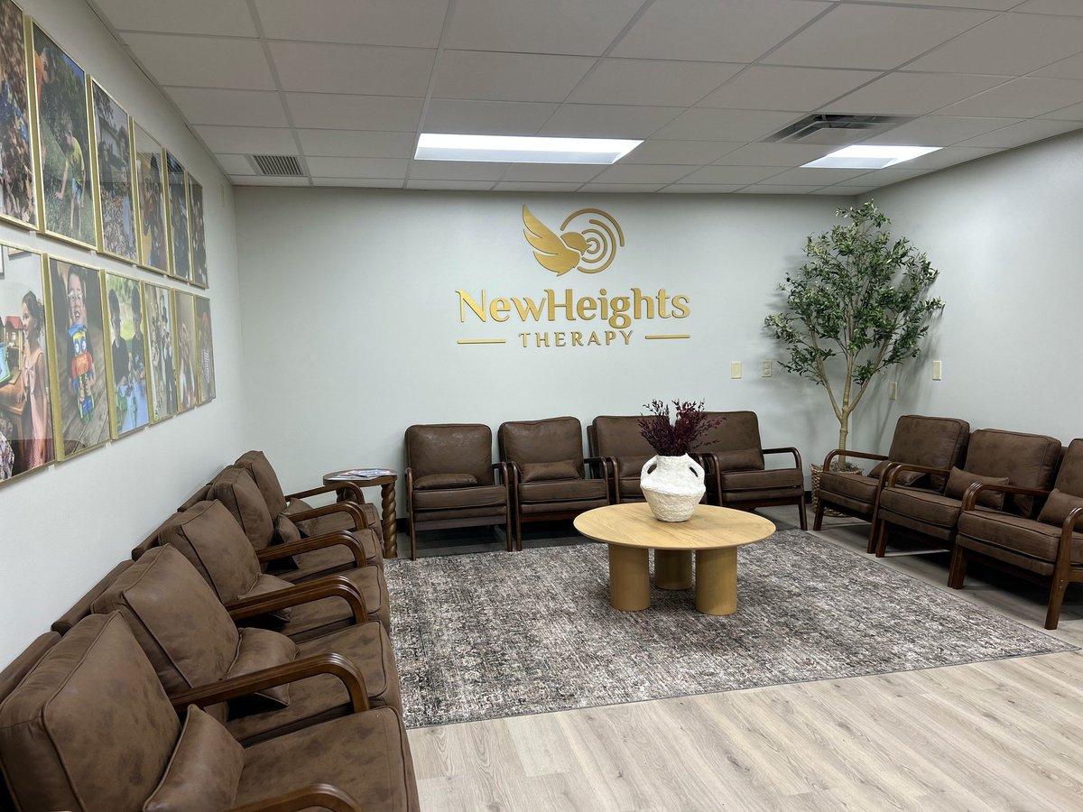 Modern therapy waiting room with brown leather recliners arranged in a circle around a wooden table with plant and New Heights Therapy logo on wall