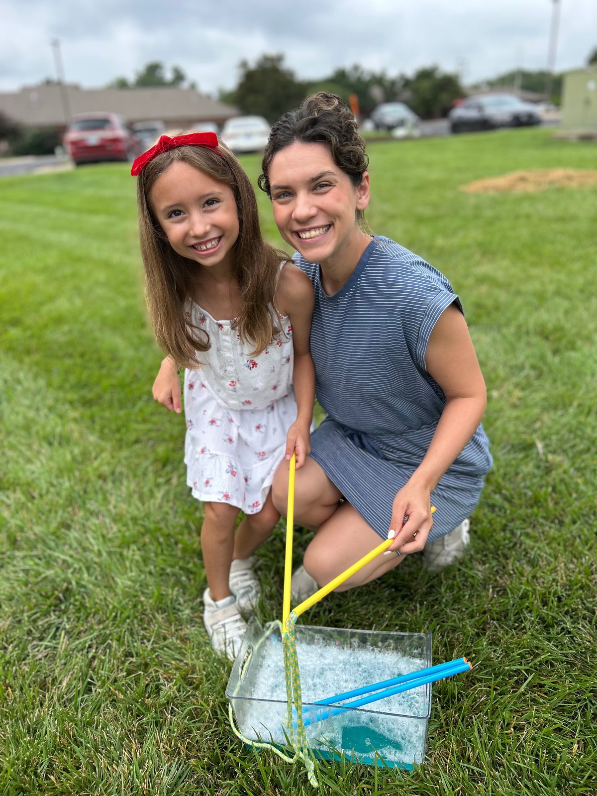Speech therapist and a young girl in a grassy field holding a bug net during outdoor, play-based speech therapy in Kansas