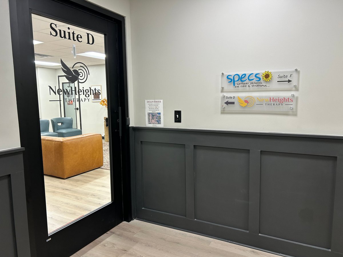 Black framed glass door to Suite D with view of office interior, yellow leather seating visible, business signs on white and dark paneled wall