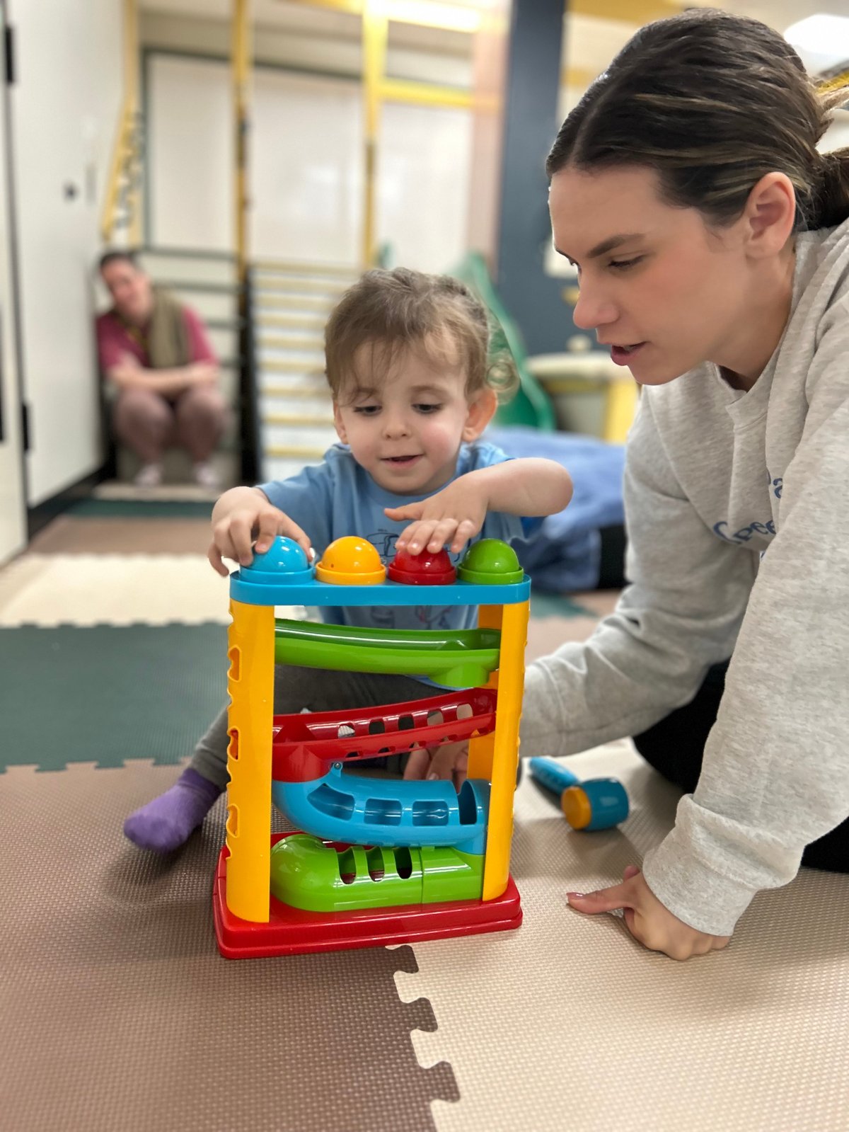 Speech therapist and a toddler playing with a colorful ball ramp toy, building early language and joint attention