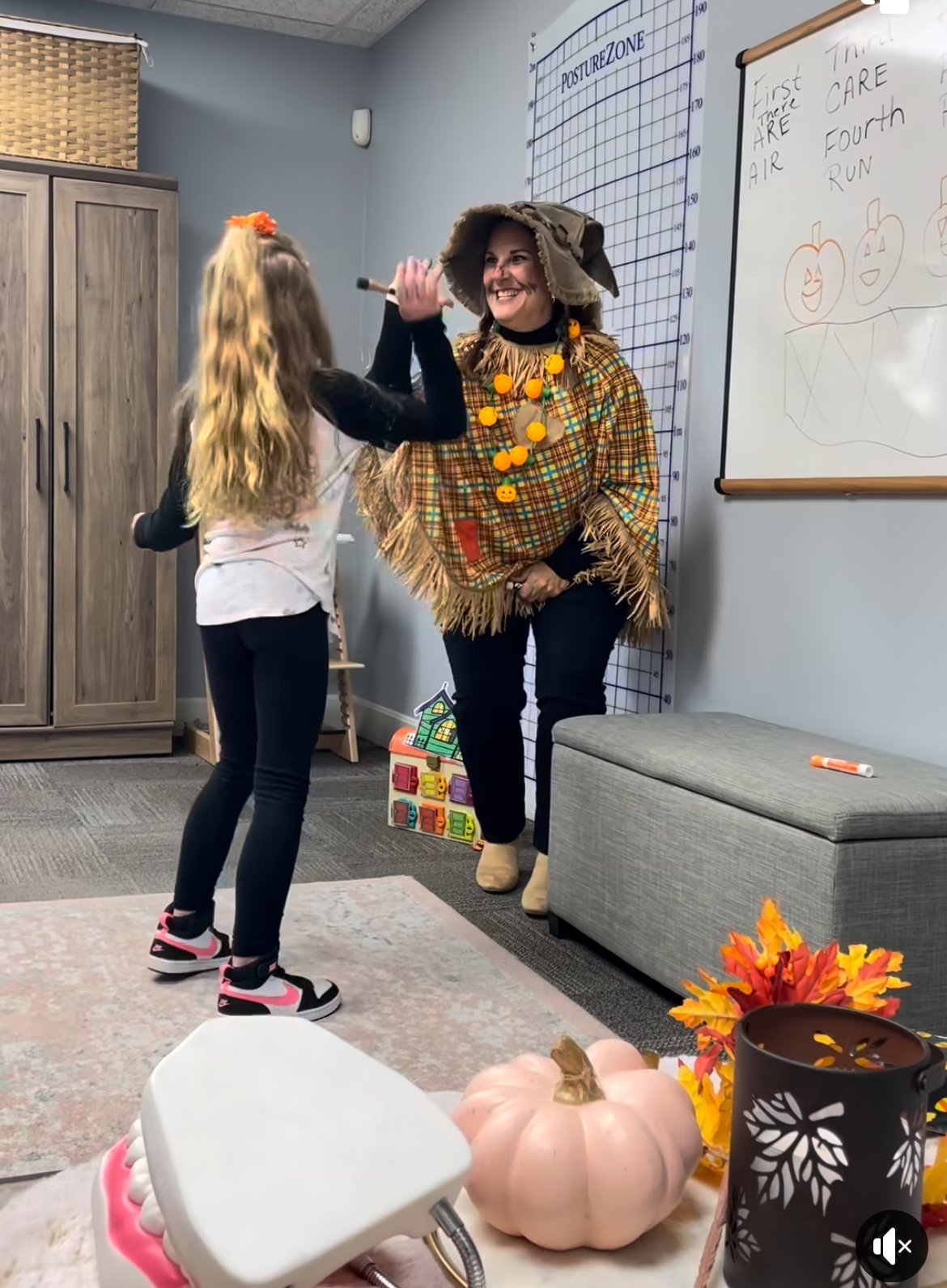 Speech therapist in a scarecrow costume giving a high-five to a child in a fall-decorated therapy room in Lawrence, KS