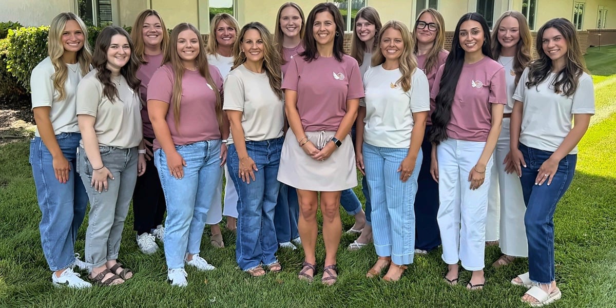 Group of women standing together on grass wearing coordinated pink and white shirts for a team photo