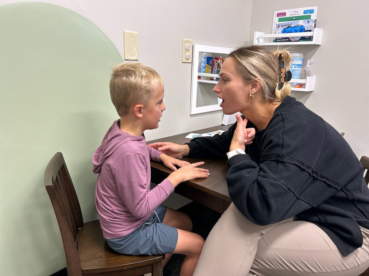 Speech therapist face to face with a young boy, exaggerating a sound so he can copy her mouth position in speech therapy