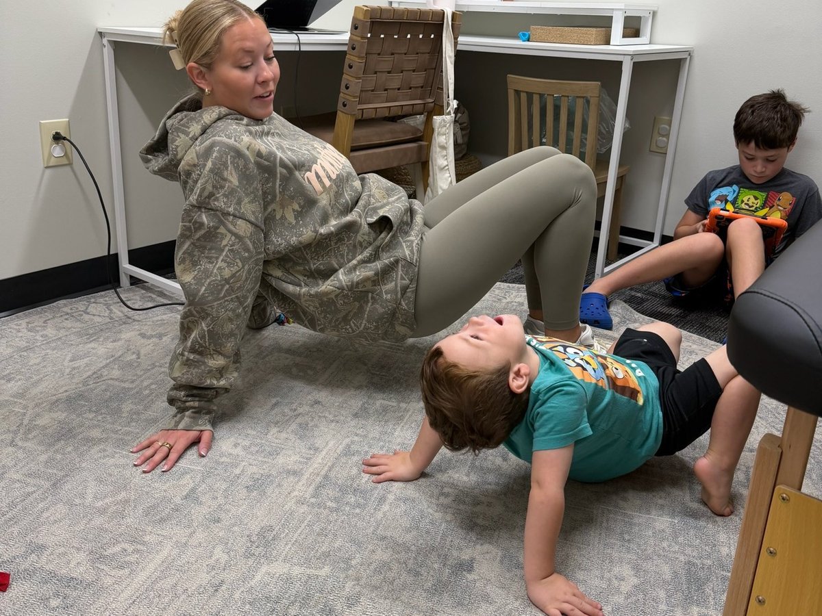 Child crab walk bridge exercise in pediatric physical therapy, building core and upper body strength with the therapist alongside