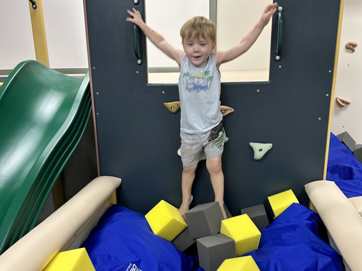 Young child with arms raised standing on foam blocks in the climbing wall pit of the sensory gym