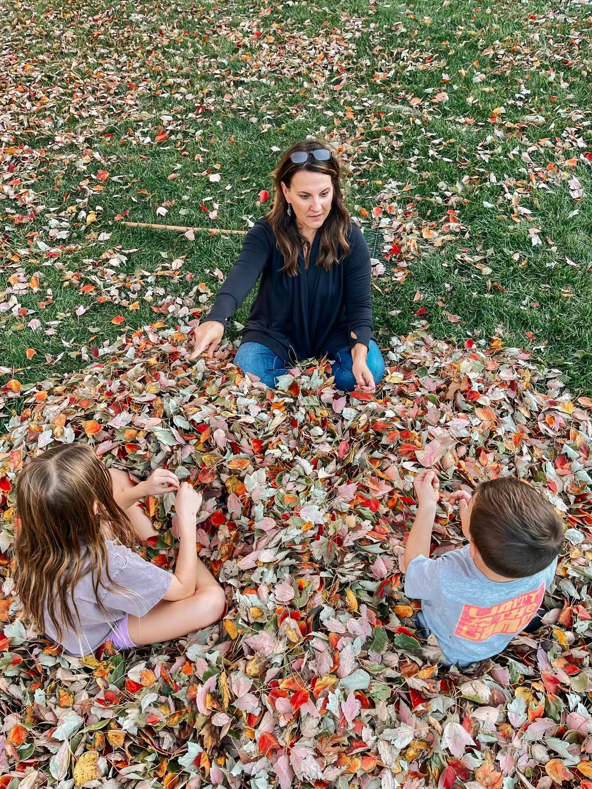 Woman and two children playing in a pile of autumn leaves on the ground